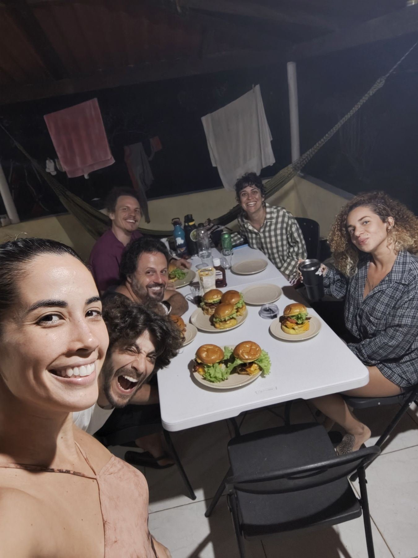 Pessoas sorrindo ao redor de uma mesa com hambúrgueres, à noite