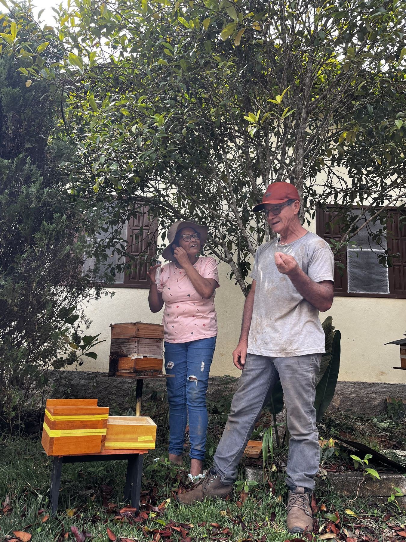 Duas pessoas conversando no quintal, ao lado de caixas de abelhas nativas